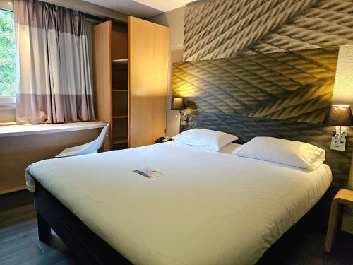 a hotel room with a large white bed with a window at Ibis Hôtel Sallanches in Sallanches