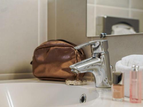 a brown purse sitting on top of a sink with a faucet at ibis Bayeux Port En Bessin in Port-en-Bessin-Huppain