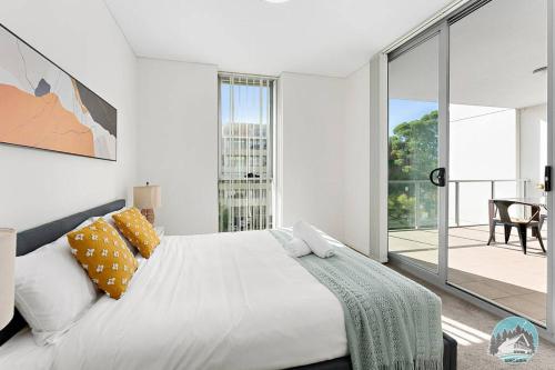 a white bedroom with a large bed and a balcony at Aircabin - Mascot - Walk to Station - 3 Beds Apt in Sydney