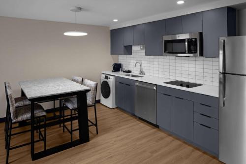 a kitchen with blue cabinets and a table and a refrigerator at Homewood Suites By Hilton Grand Prairie At EpicCentral in Grand Prairie