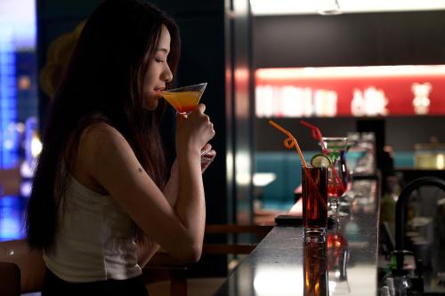 a woman sitting at a bar drinking a drink at Lan Wan Hotel - Next to Huangsha Metro St ation -One cup of Free Cockt ail or Harbin Beer Per Room--Cha rgeable Airport Pick-up Service in Guangzhou
