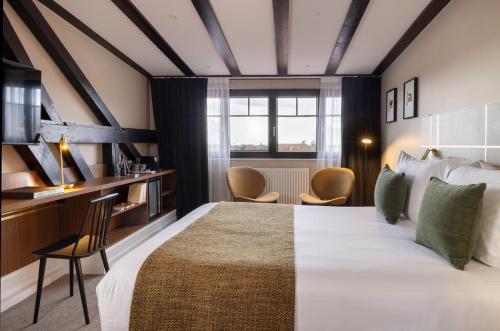 a bedroom with a large bed and a desk and chairs at Hotel Le Colombier in Obernai