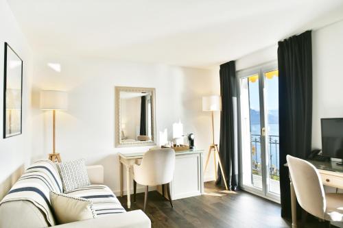 ein Wohnzimmer mit einem Sofa, einem Schreibtisch und einem TV in der Unterkunft Baron Tavernier Hotel Restaurant & SPA in Chexbres