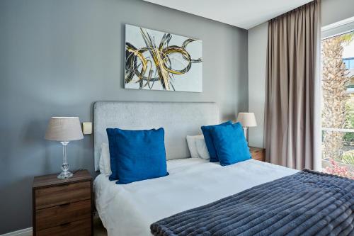 a bedroom with a bed with blue pillows and a window at Spacious Apartment Waterfront Fast WIFI in Cape Town