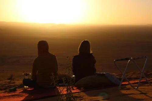 two people sitting on a hill watching the sunset at Auberge Dinosaur Kem Kem in Tafraoute Sidi Ali