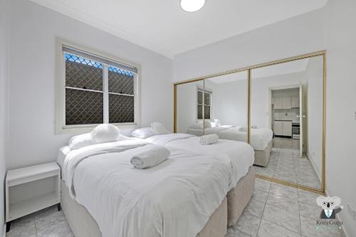 a white bedroom with two beds and a large mirror at Fairfield 1B Granny Flat Sleep up to 4 ppl in Fairfield