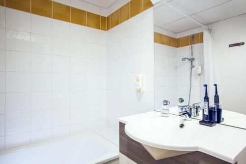 uma casa de banho branca com um lavatório e uma banheira em Aparthotel Adagio Access Nogent sur Marne em Nogent-sur-Marne