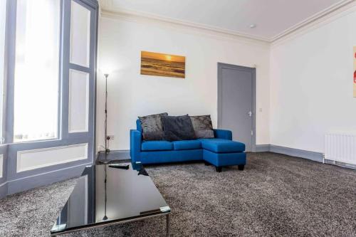 a living room with a blue couch and a table at Guest Homes - Bambro Flat in Sunderland