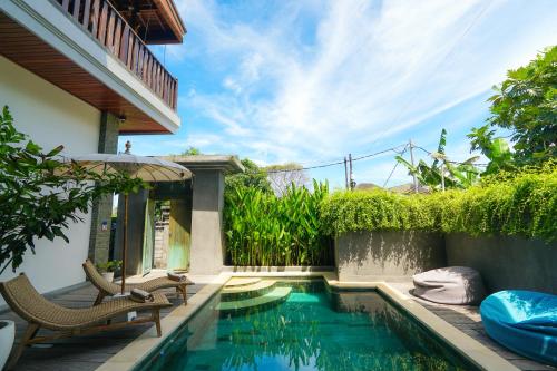 Tropical Beach House Bali في سمينياك: مسبح مع كراسي ومظلة بجانب منزل