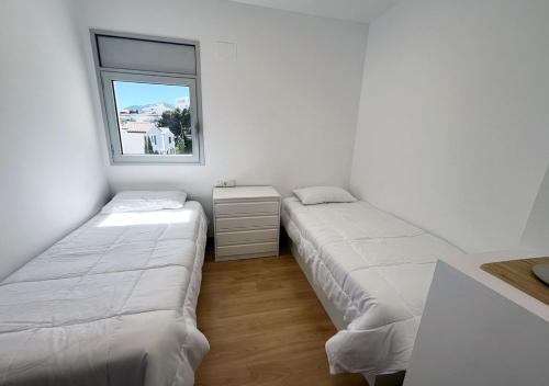 two beds in a white room with a window at 2-bedroom brand new apartment steps from the beach in Llança