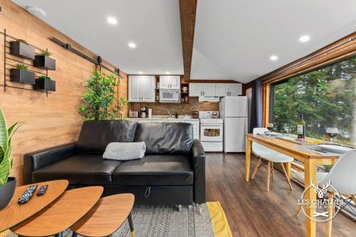 a living room with a black leather couch and a kitchen at Le1613 - Bord de l'eau - Les chalets dans le nord in Val-David