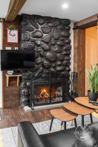 a living room with a stone fireplace with two tables at Le1613 - Bord de l'eau - Les chalets dans le nord in Val-David