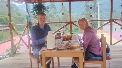 a man and a woman sitting at a table with food at the wooden house choquequirao in Cachora