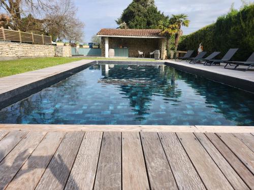 a swimming pool with a wooden deck and a house at Domaine de Quittignan Brillette in Moulis-en-Médoc