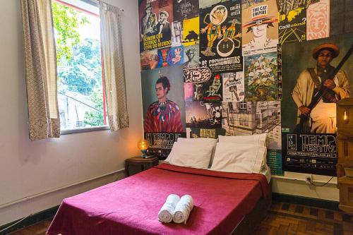 1 dormitorio con 1 cama con una manta rosa y carteles en Mambembe Hostel, en Río de Janeiro