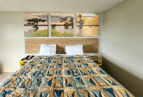 a bedroom with a bed with three paintings on the wall at Days Inn by Wyndham Lafayette Scott in Lafayette