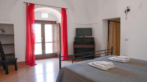 a bedroom with a bed with red curtains and a television at Vineyard View, Garden & BBQ - Historic "Dammusi" in Pantelleria