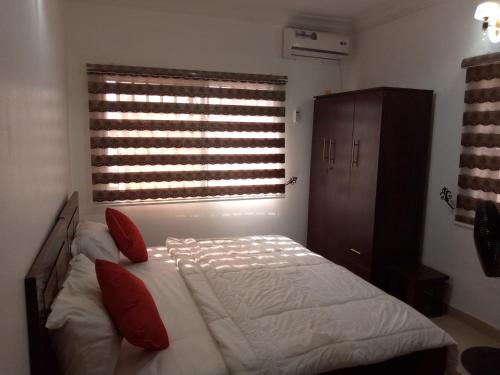 a bedroom with a bed with red pillows and a window at Cossy Luxury Hotel and Apartments in Galadima