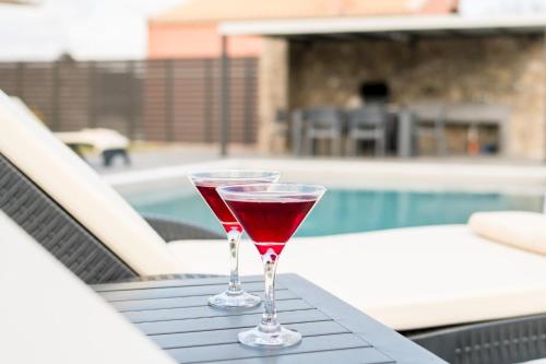 two glasses of red wine sitting on a table next to a pool at Castelia Luxury Villas in Agios Ioannis