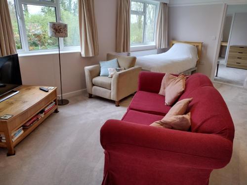 a living room with a red couch and a bed at Robin Hill Cottage in Amesbury