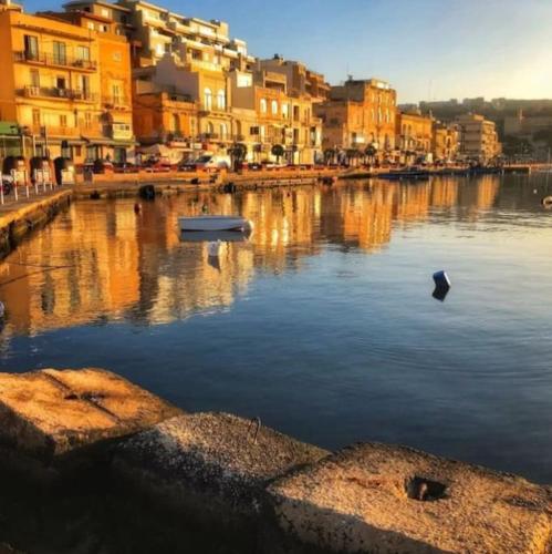 a river with buildings and a boat in the water at Penthouse with Picturesque Garden and Bayviews in Marsaskala