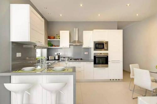 a kitchen with white cabinets and white appliances at Penthouse with Picturesque Garden and Bayviews in Marsaskala