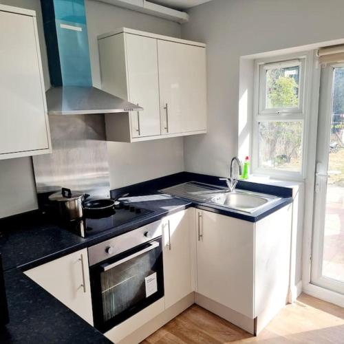 a kitchen with white cabinets and a sink and a stove at Stylish Apartment, self check-in, Ideal 4 Contractors, 25mins to Gatwick Airport in Thornton Heath