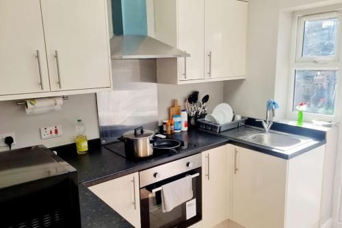 a kitchen with white cabinets and a black counter top at Stylish Apartment, self check-in, 25mins to Airport in Thornton Heath