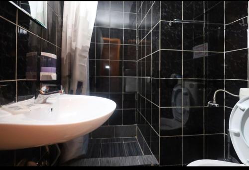 a black tiled bathroom with a sink and a toilet at Uptown Inn in Sarajevo