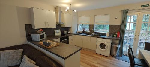 a kitchen with white cabinets and a living room at Ben Reoch Cottage - Loch Lomond and Arrochar Alps in Tarbet