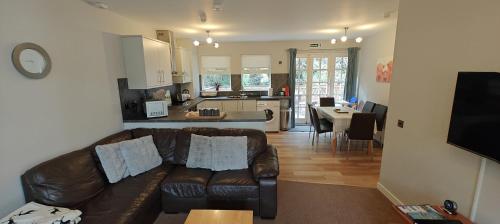 a living room with a leather couch and a kitchen at Ben Reoch Cottage - Loch Lomond and Arrochar Alps in Tarbet