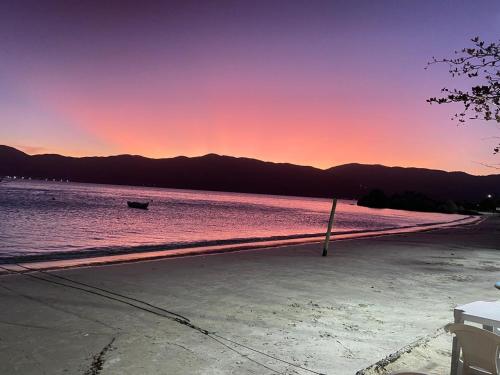 a beach with a boat in the water at sunset at Residencial Marémansa pousada apto 01 in Governador Celso Ramos