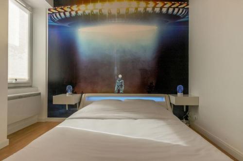 une chambre avec un lit blanc avec un tableau sur le mur dans l'établissement La Zone 51, à Orléans