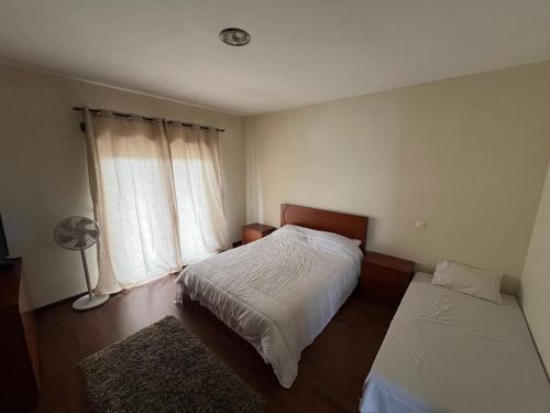 a bedroom with a bed and a window with a fan at Casa Rosa Aluguel de Quartos in Calvão