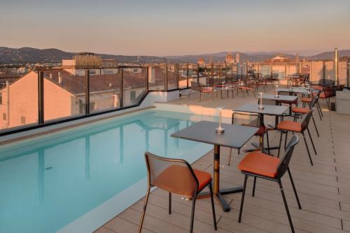 a rooftop patio with tables and chairs next to a swimming pool at NH Firenze in Florence