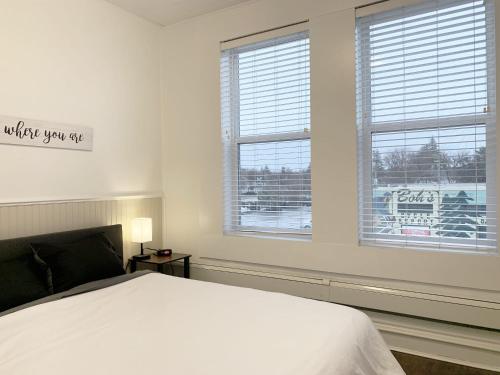 a white bedroom with a bed and two windows at Gorgeous 1-bedroom Condo Location WiFi in Moose Jaw
