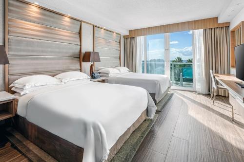 two beds in a hotel room with a large window at Hilton at Resorts World Bimini in Alice Town