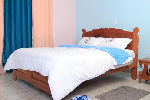 a bedroom with a wooden bed with white sheets at Koma Gardens and Resort in Nguluni