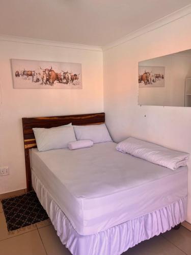 una camera da letto con un letto con lenzuola bianche e dipinti di Comfort Guesthouse a Windhoek