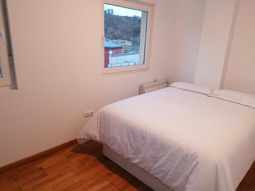 ein kleines Schlafzimmer mit einem weißen Bett und einem Fenster in der Unterkunft Dúplex Unquera. Piscina, garaje. in Unquera