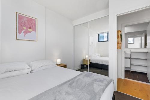 a white bedroom with a bed and a mirror at Cosy 1-Bed with Private Balcony By Showgrounds in Melbourne