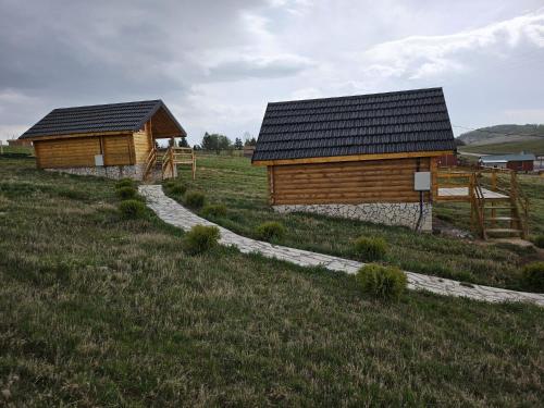 two wooden buildings in a field with a grass field at Etno selo Raj na Uvcu in Sjenica
