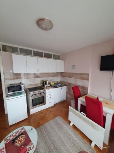 a kitchen with white cabinets and a table and red chairs at Apartman Centar in Bijeljina