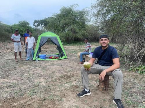 a man sitting on a tree stump in front of a tent at Black Panther Yala in Tissamaharama