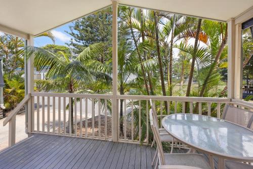 a porch with a glass table and chairs and palm trees at Reflections Tuncurry - Holiday Park in Tuncurry