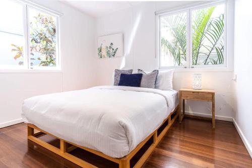 a bedroom with a large bed with white sheets and windows at 'The Otto' At Moffat Beach in Caloundra