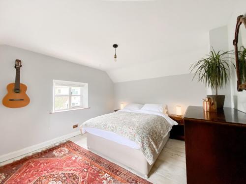 a white bedroom with a bed and a guitar at Oasis Cottage in Broughton Gifford