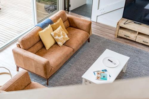 a brown couch sitting in a living room at The Glass House 103 Bristow-Smith Ave Goolwa South - BYO Linen in Goolwa South