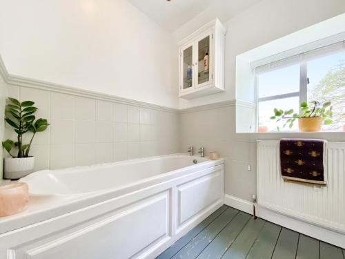 a white bathroom with a tub and a window at Oasis Cottage in Broughton Gifford