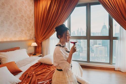 una mujer sosteniendo una copa de vino en una habitación de hotel en Nanyang-French Autumn Movie Scene With KLCC View, en Kuala Lumpur
